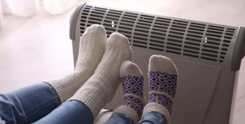 Two sets of feet up against an electric space heater